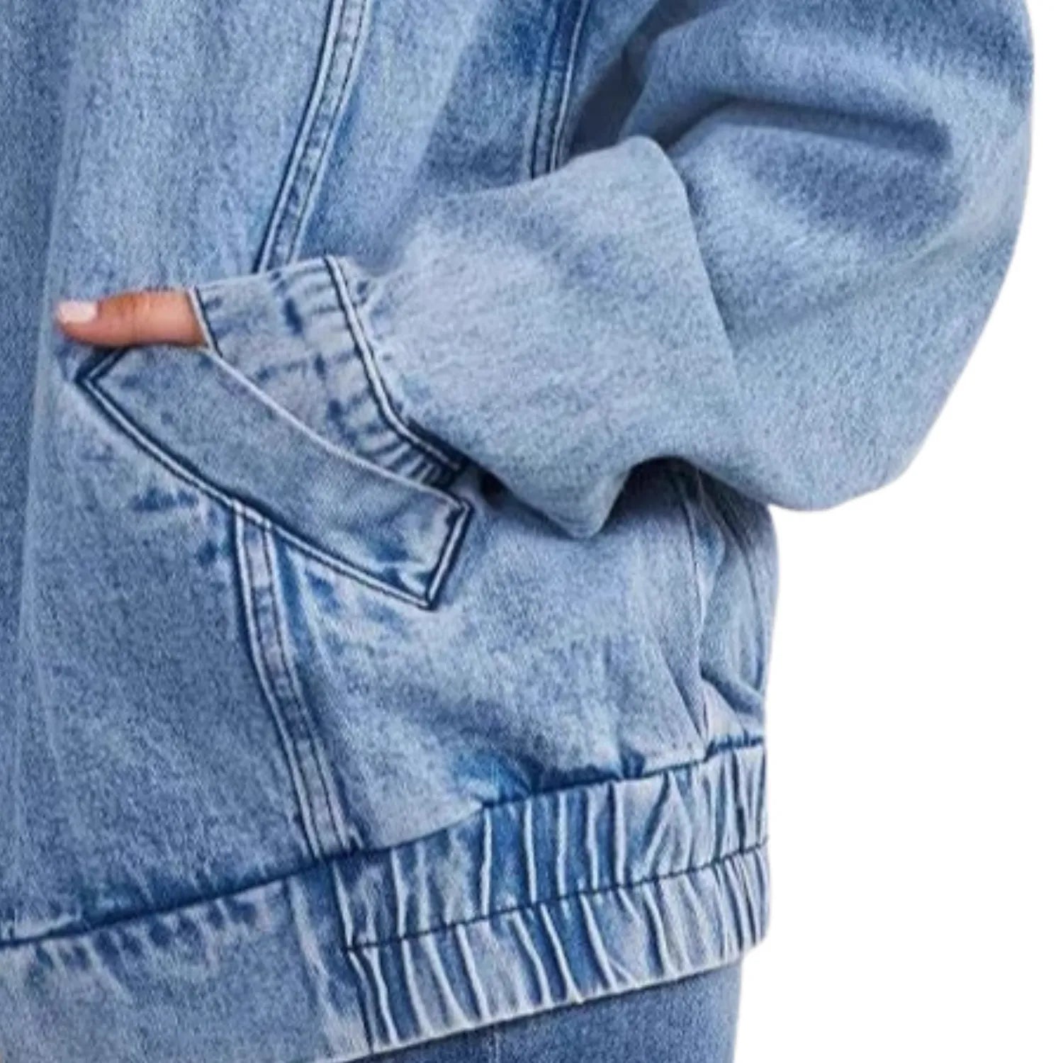 Close-up of the denim jacket's side pocket, highlighting the classic stitching and elastic hem detail.