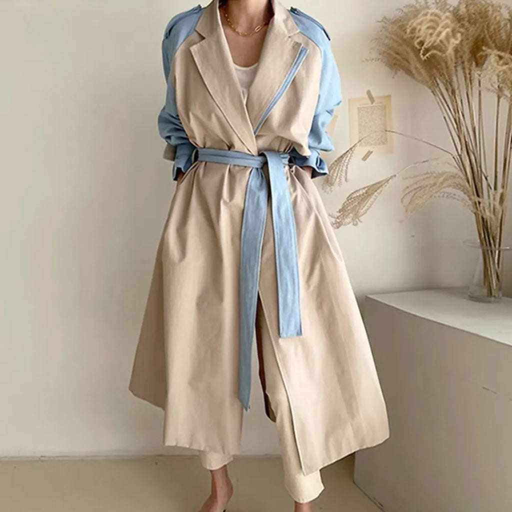 Women's Retro Lapel Trench Coat beige, highlighting the contrasting fabric panels, deep pockets, and long, flowing silhouette.