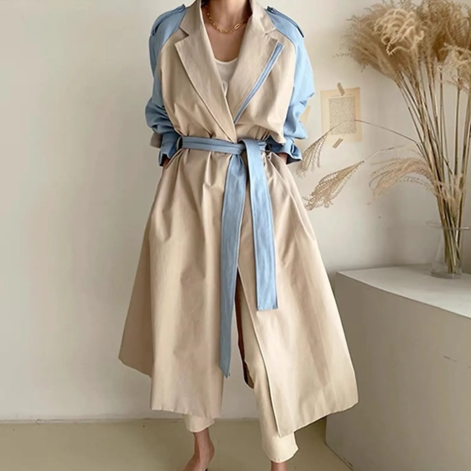 Women's Retro Lapel Trench Coat beige, highlighting the contrasting fabric panels, deep pockets, and long, flowing silhouette.